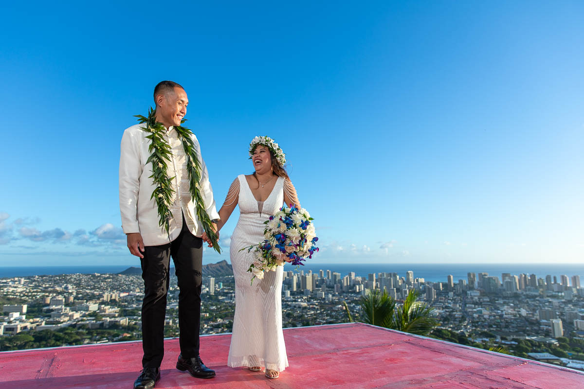 Bride and Groom holding each other's hands in their wedding attire near the outlook of Honolulu.