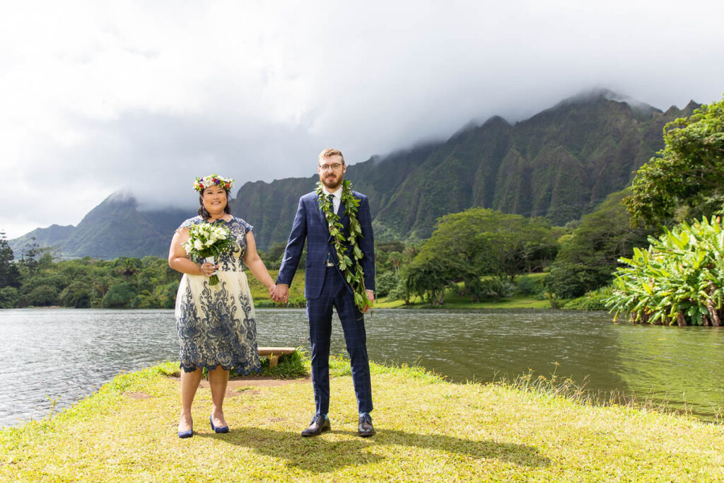 Wedding couple holding hands in front of lake and Ko'olau mountains